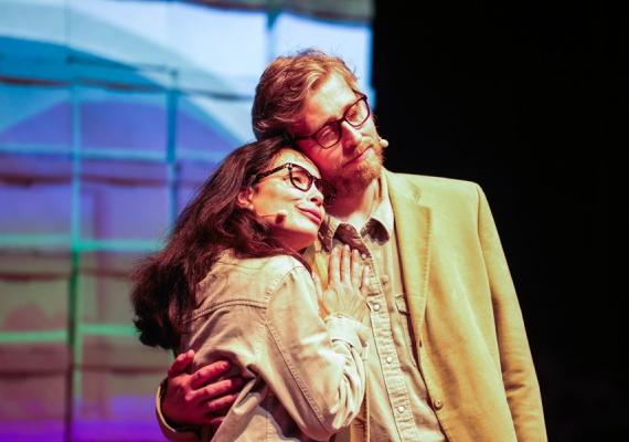 Two actors embrace in front of colorful screen